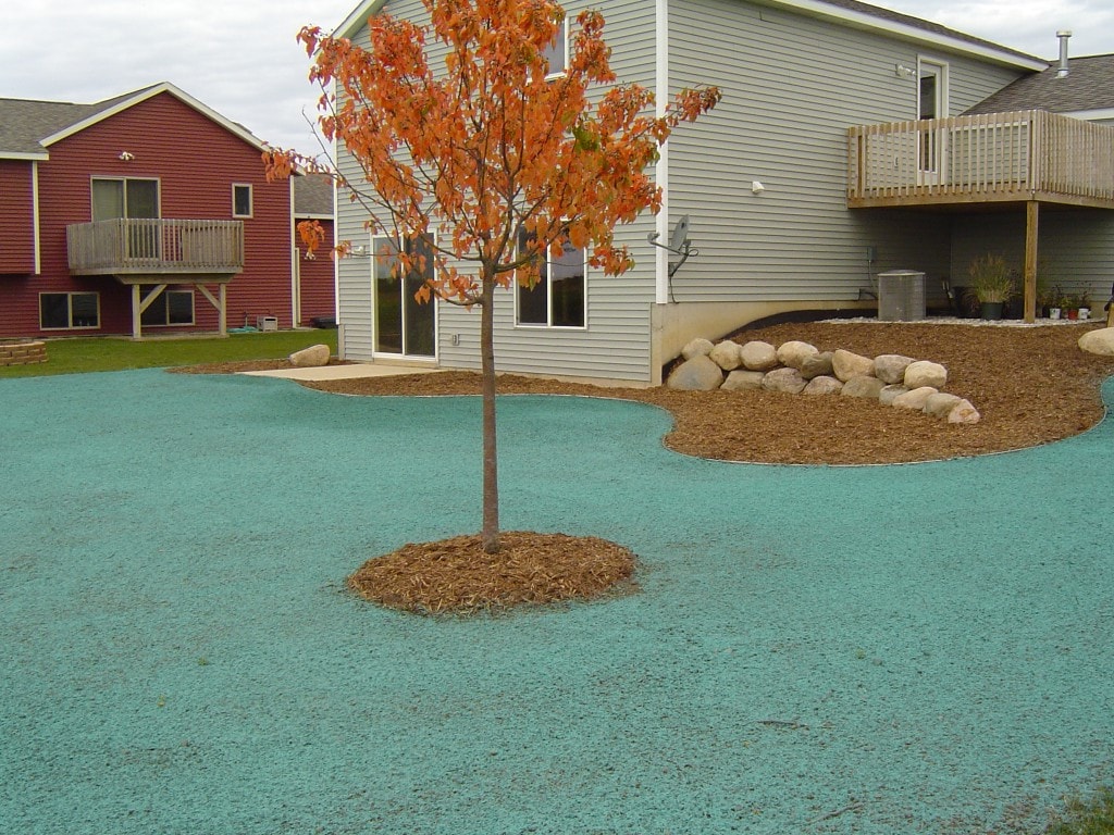 Backyard with newly planted tree, boulder retaining wall, and fresh hydroseed